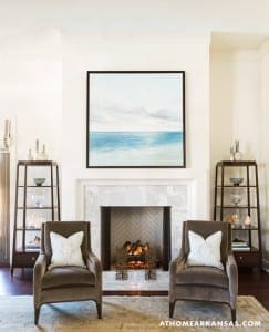 Gray upholstered armchairs flank a marble fireplace in a living room.