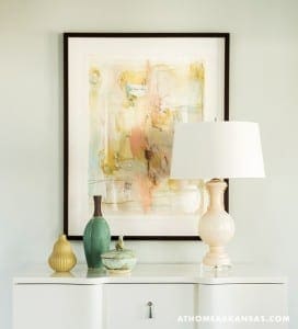 White console table with artwork, lamp, and decorative vases.