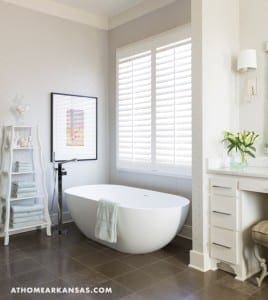 White bathroom with a freestanding tub, shutters, and shelving.