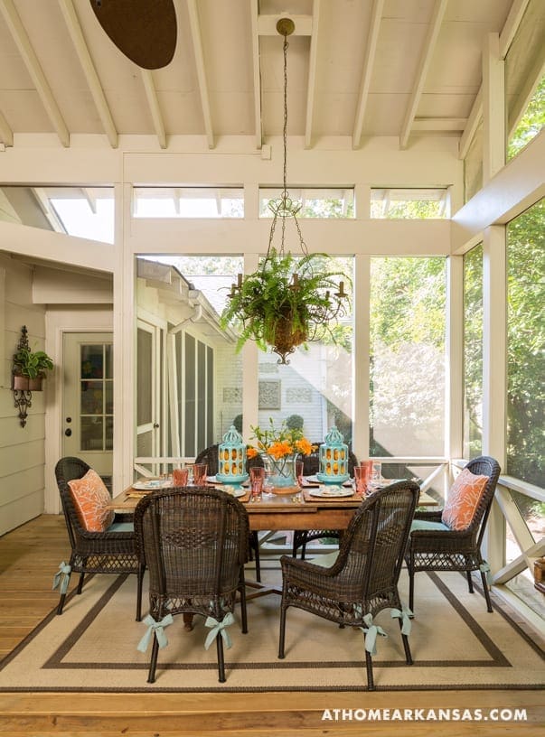 White screened porch with dining table and chairs, hanging light fixture.