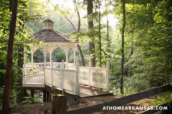White gazebo on a wooden bridge in a wooded area.