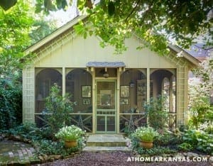 Yellow cottage with screened porch, surrounded by greenery.