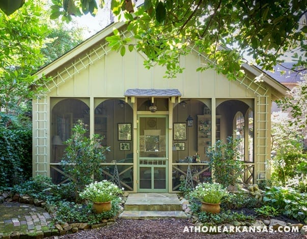 Yellow cottage with screened porch, surrounded by greenery.