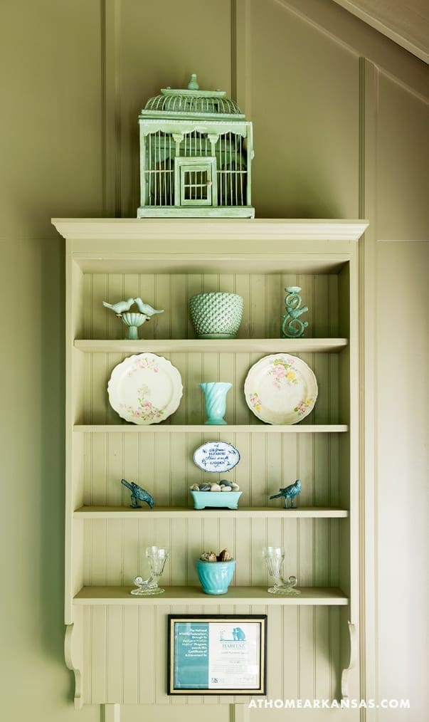 Green shelving unit with decorative birdhouse and ceramics.