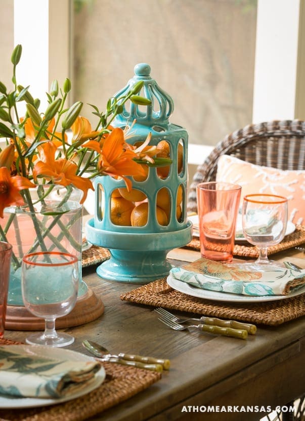 Turquoise lantern with orange lilies on a wooden table.
