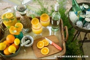 Tray with citrus drinks, ice, and fruit on a bamboo surface.