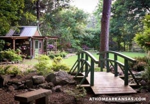 Green wooden bridge and small shed in a wooded landscape.