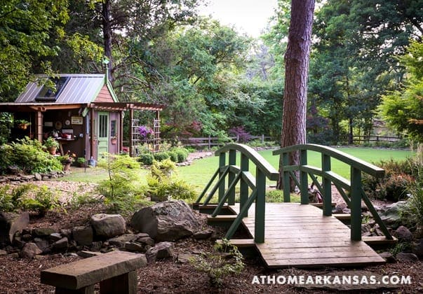 Green wooden bridge and small shed in a wooded landscape.