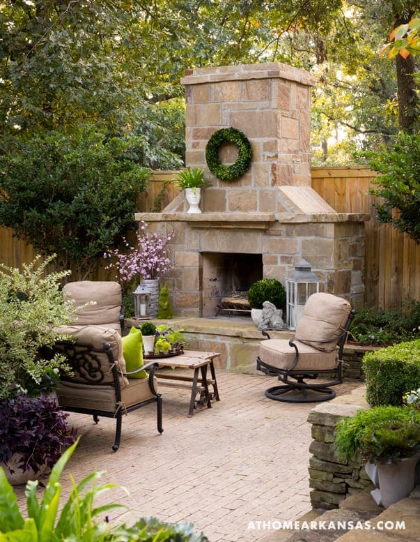 Stone outdoor fireplace with seating and greenery.