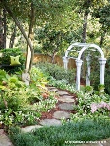 White archway in garden with stone pathway and foliage.