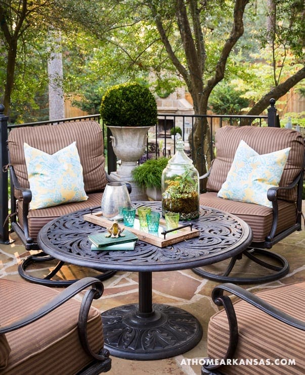 Patio with brown chairs, table, and greenery.