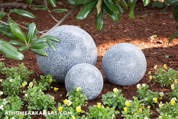 Three gray concrete spheres in a garden setting.