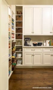 White walk-in pantry with shelves, baskets, and appliances.