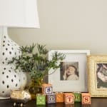 White lamp, wooden blocks, framed photos on dark console.