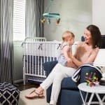 Woman holding baby in a nursery with striped curtains and a mobile.