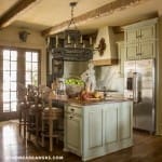 Kitchen with light green cabinetry, wooden island, and exposed beams.
