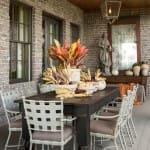 Brick porch with a wooden table, chairs, and fall foliage.