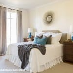 White bedroom with a wooden bed, curtains, and a round mirror.