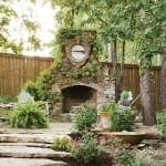 Stone fireplace with ivy and a circular window, surrounded by plants and a wooden fence.