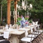 Outdoor dining table with a large chandelier and floral centerpiece.
