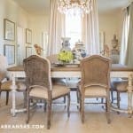 Dining room with a white table, rattan chairs, and a crystal chandelier.