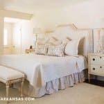 White bedroom with a carved headboard, dresser, and bench.