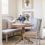 Cream-colored bench with pillows, table, and chair in a dining nook.