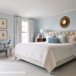 Blue bedroom with a tufted headboard, artwork, and furniture.