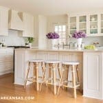 White kitchen with island, brass accents, and wooden stools.