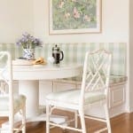 White banquette with striped upholstery, wicker chairs, and floral artwork.