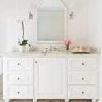 White vanity with marble countertop, mirror, and floral arrangement.