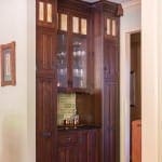 Dark wood cabinetry with glass-fronted shelving and tiled backsplash.