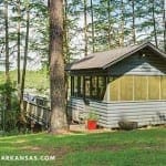 Gray lakeside pavilion with a wooden deck and windows.