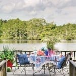 Deck with table, chairs, and outdoor dining set by a lake.