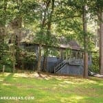 Gray cottage with porch, surrounded by trees and lawn.