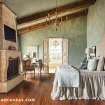 Bedroom with stone fireplace, wooden beams, and pale green walls.