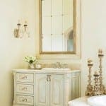 Light-colored vanity with marble countertop and faucet, flanked by candlesticks and a mirror.