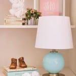 White lamp with turquoise base, wooden boots, and books.