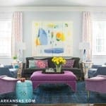 Gray wall with abstract art, purple armchairs, and a purple ottoman.