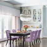 White dining room with purple chairs, cabinets, and a chandelier.