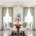 Formal dining room with light blue drapes, chandelier, and wooden table.