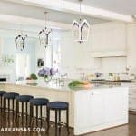 White kitchen with island, dark stools, and pendant lighting.