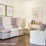 Gray upholstered bench with gold bar cart and artwork.