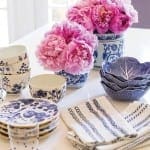 Pink peonies in a blue and white patterned vase with plates and napkins.