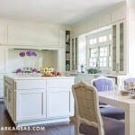 White kitchen with an island, wood table, and floral arrangements.