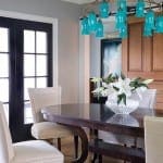 Dining room with teal chandelier, wooden table, and floral arrangement.