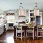 White kitchen with a dark island and patterned chairs.