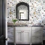 White vanity with patterned wallpaper featuring butterflies, a mirror, and sconces.