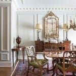 White paneled room with antique furniture, mirror, and chandelier.