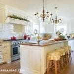 White kitchen with island, brass chandelier, and tile backsplash.